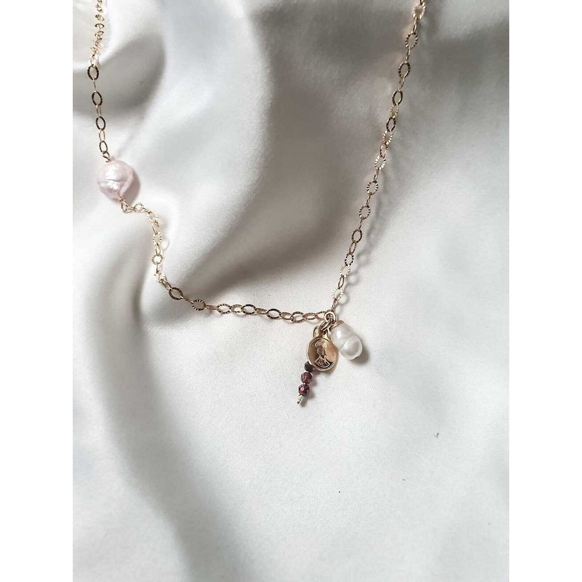 A gold necklace with a pink pearl, a pendant of white pearl and a garnet